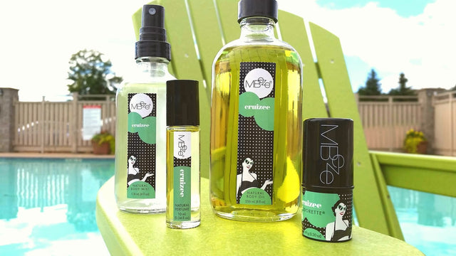 MBeze Cruizee Collection including Body Mist, Perfume, Body Oil, and Deodorette on a big green chair, poolside.